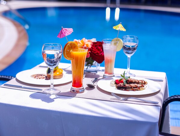 Una mesa preparada con bebidas y un plato de comida junto a una piscina.