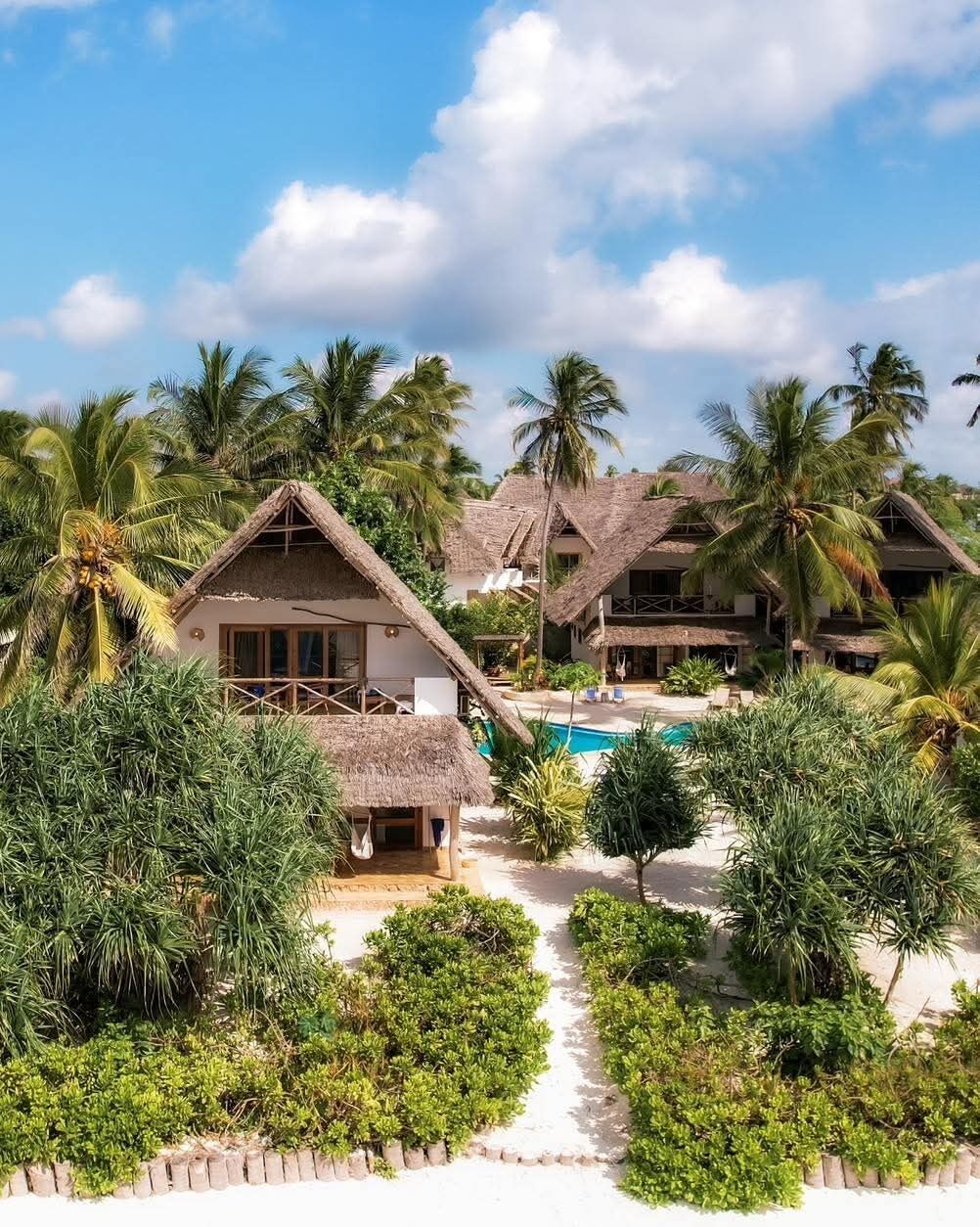 A resort with thatched-roof buildings, a swimming pool, and tropical vegetation.