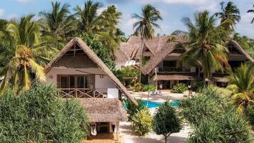 A resort with thatched-roof buildings, a swimming pool, and tropical vegetation.