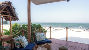 A wooden deck with two cushioned chairs, a woven hanging light fixture, and a view of the beach. - Marafiki Beach Hotel & Spa (Matemwe)
