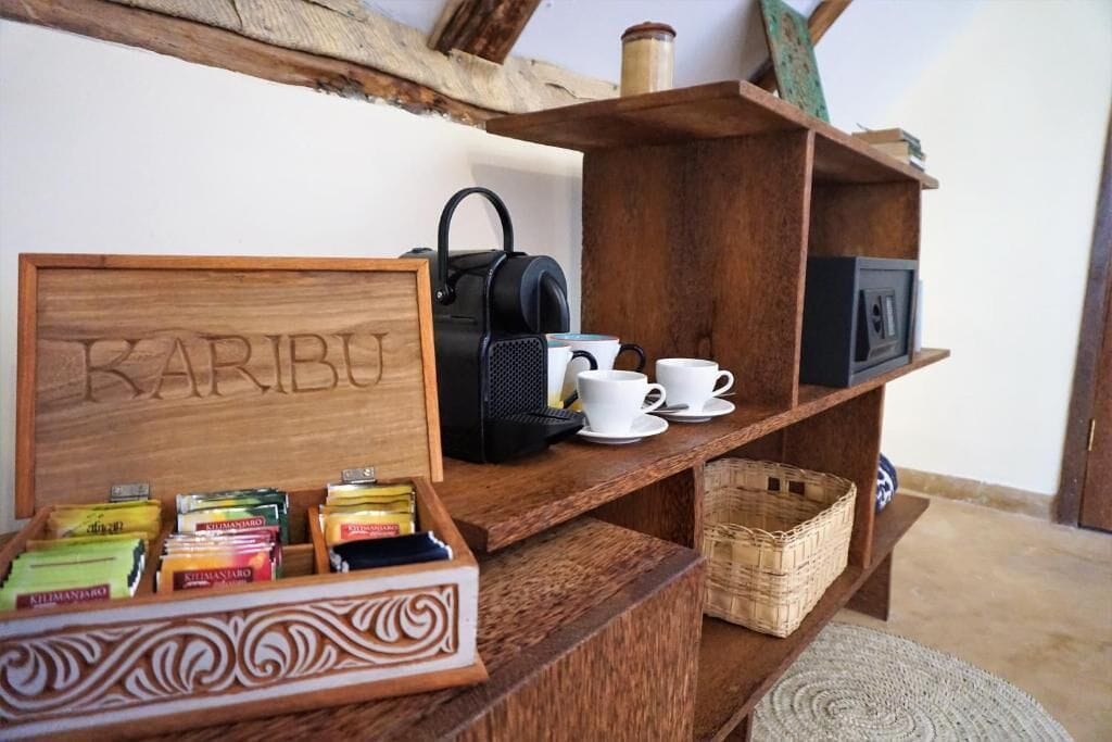 A wooden shelf with a coffee maker, cups, and a box labeled "KARIBU".
