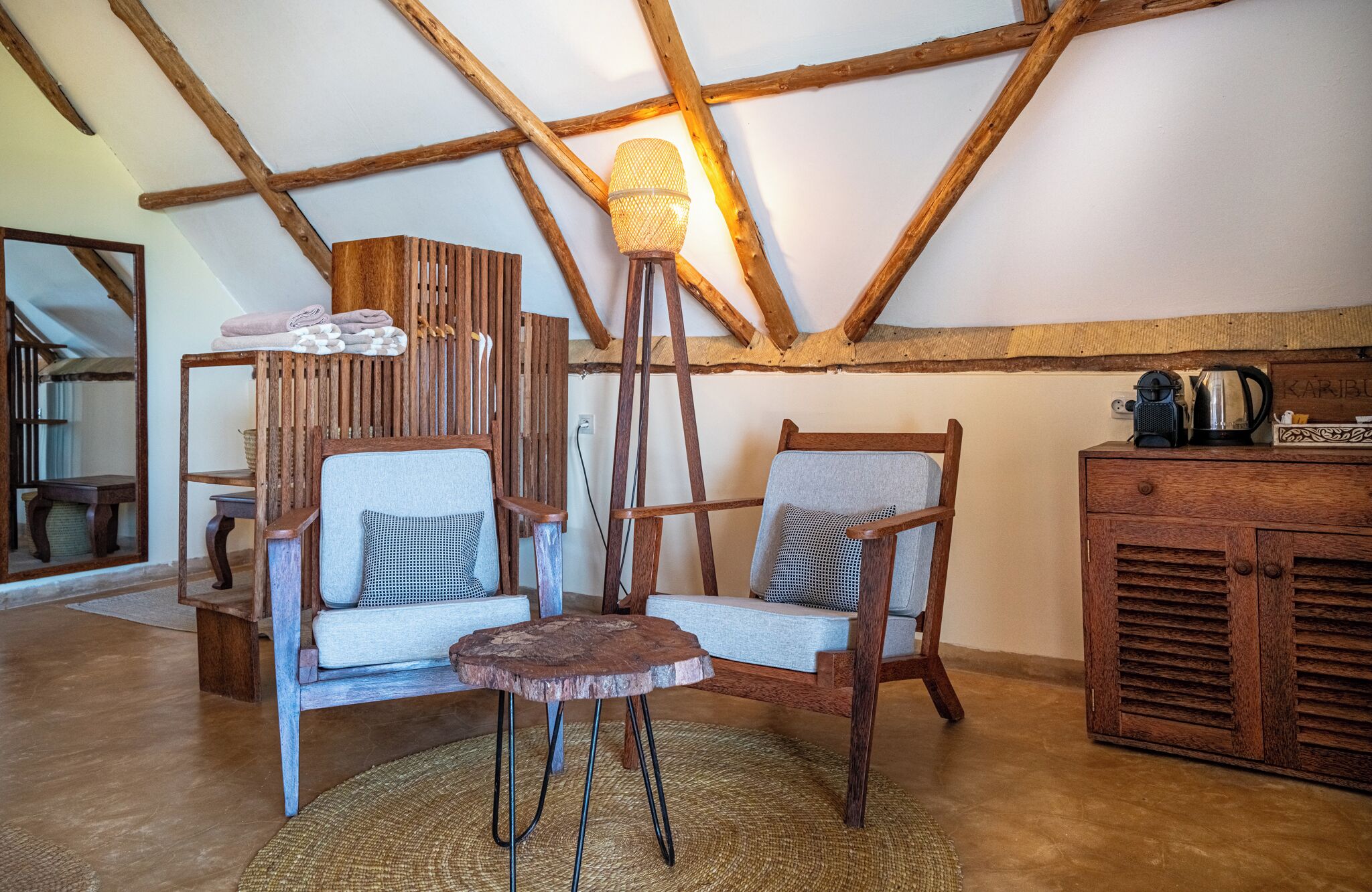 Una habitación rústica con vigas de madera, dos sillones tapizados, una mesita redonda y un aparador de madera.