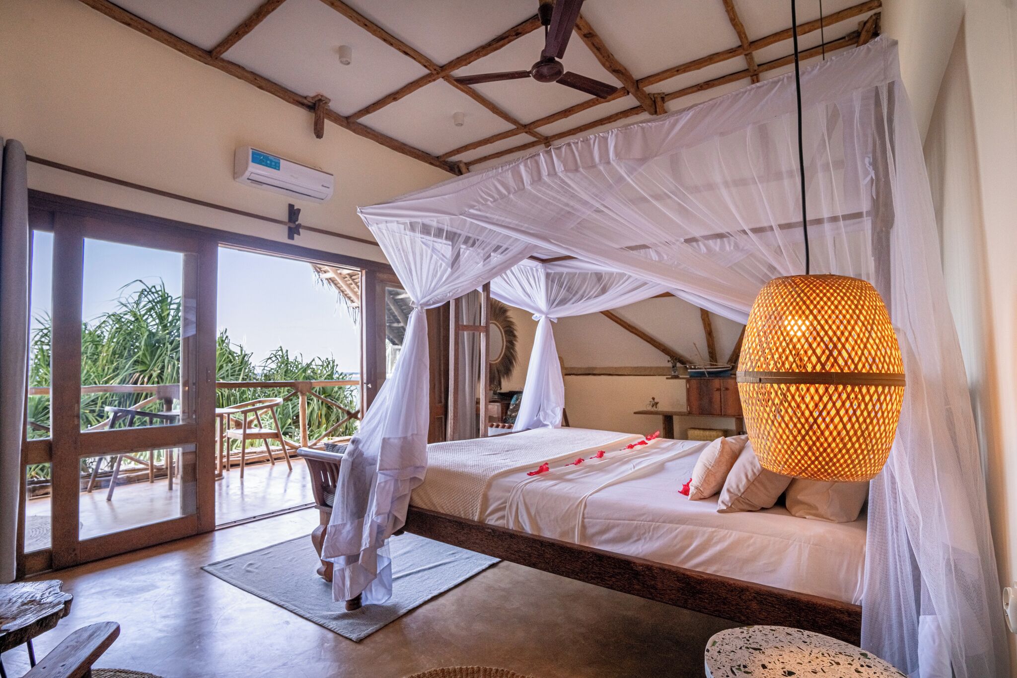 A bedroom with a bed under a white canopy, a wooden ceiling, and a large window.