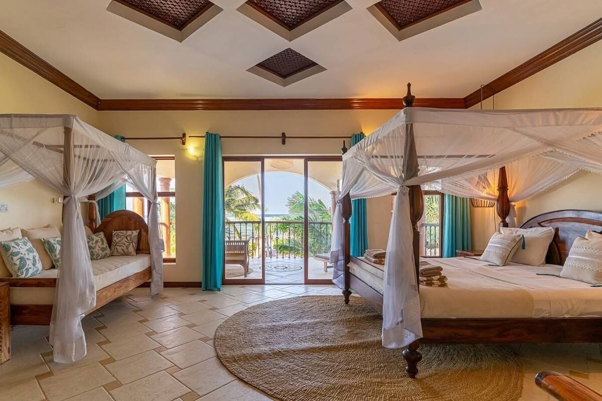 A room with a bed, a bench, a large window, and a view of the outdoors.