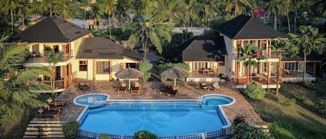 A resort with a swimming pool, multiple guest rooms, and a tropical setting with palm trees.