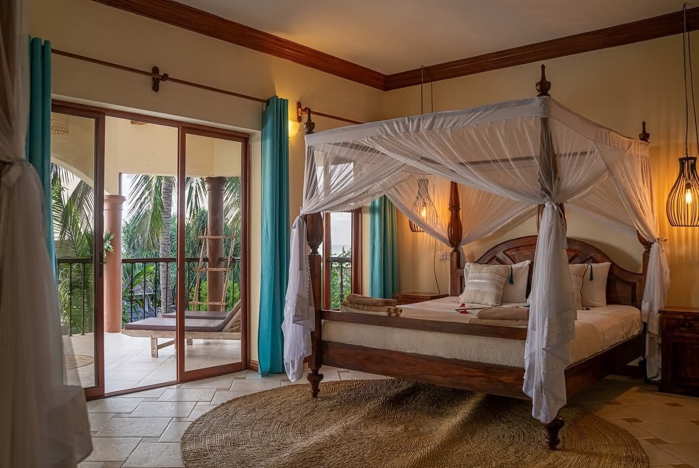 A bedroom with a four-poster bed, a balcony with a view of palm trees, and a sliding glass door.