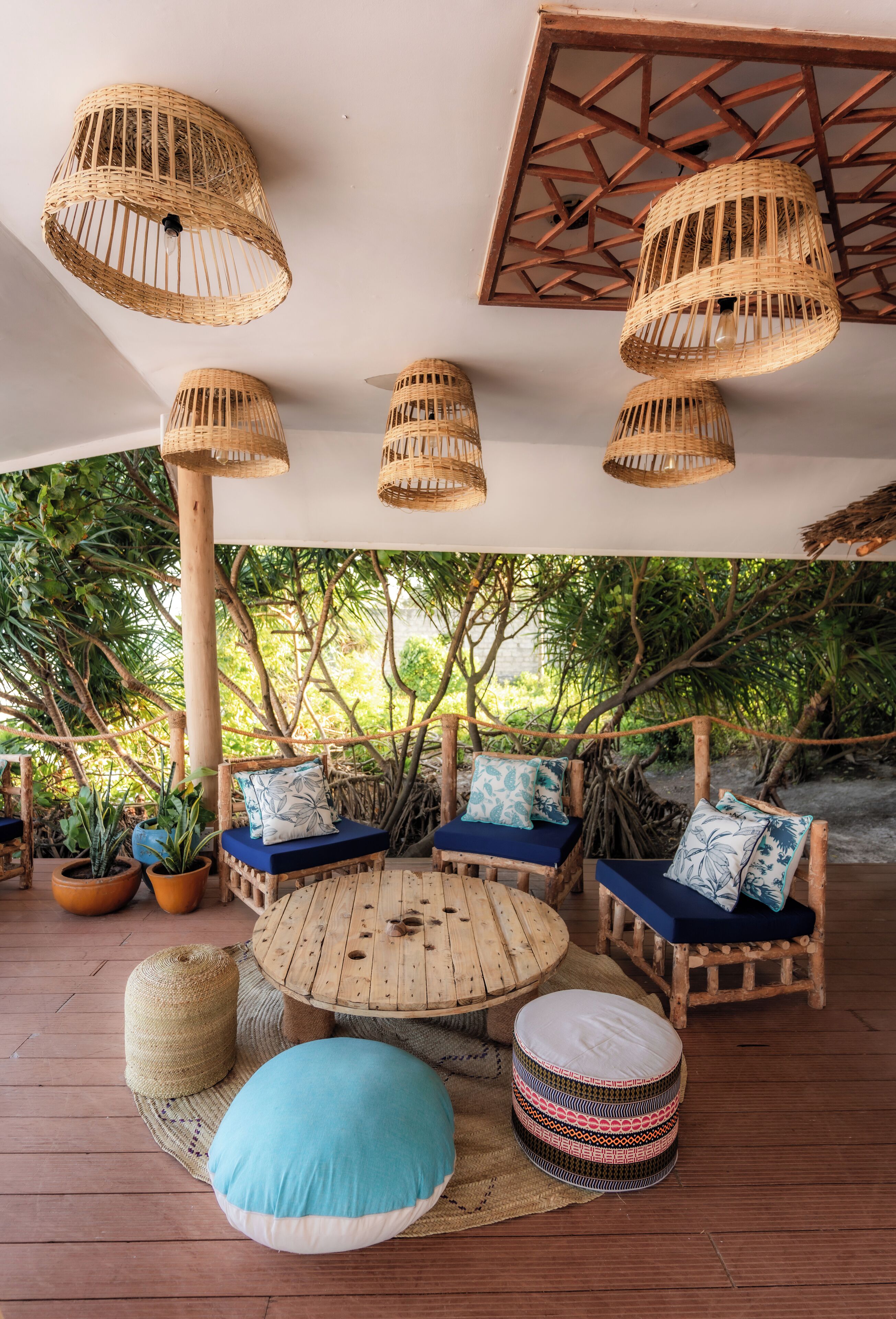 Un espacio de estar al aire libre cubierto con lámparas de mimbre, mobiliario de madera y plantas en macetas.
