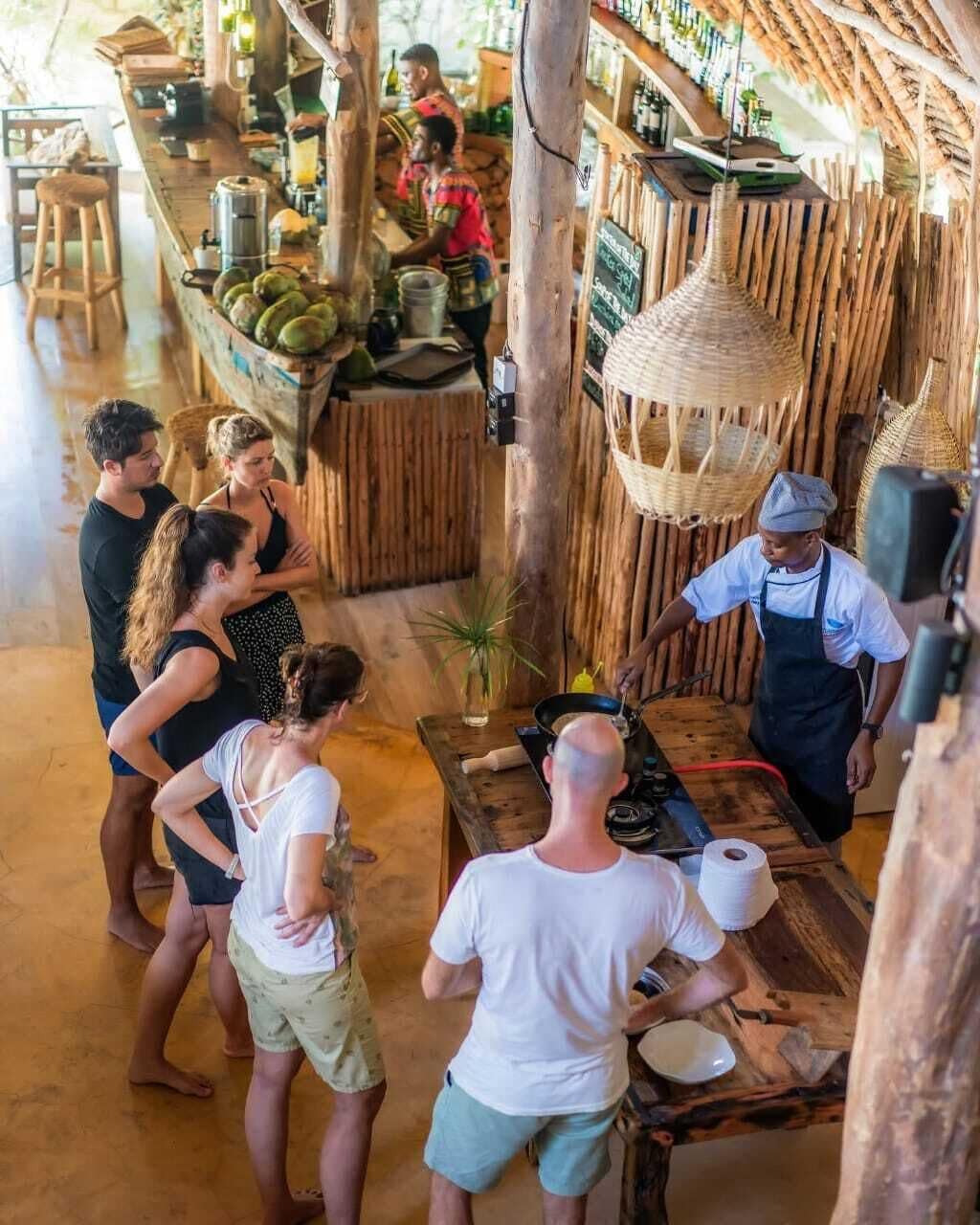 Un interior rústico con una barra de madera, una cesta colgante y una persona cocinando en la barra.