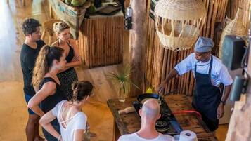 Un interior rústico con una barra de madera, una cesta colgante y una persona cocinando en la barra.