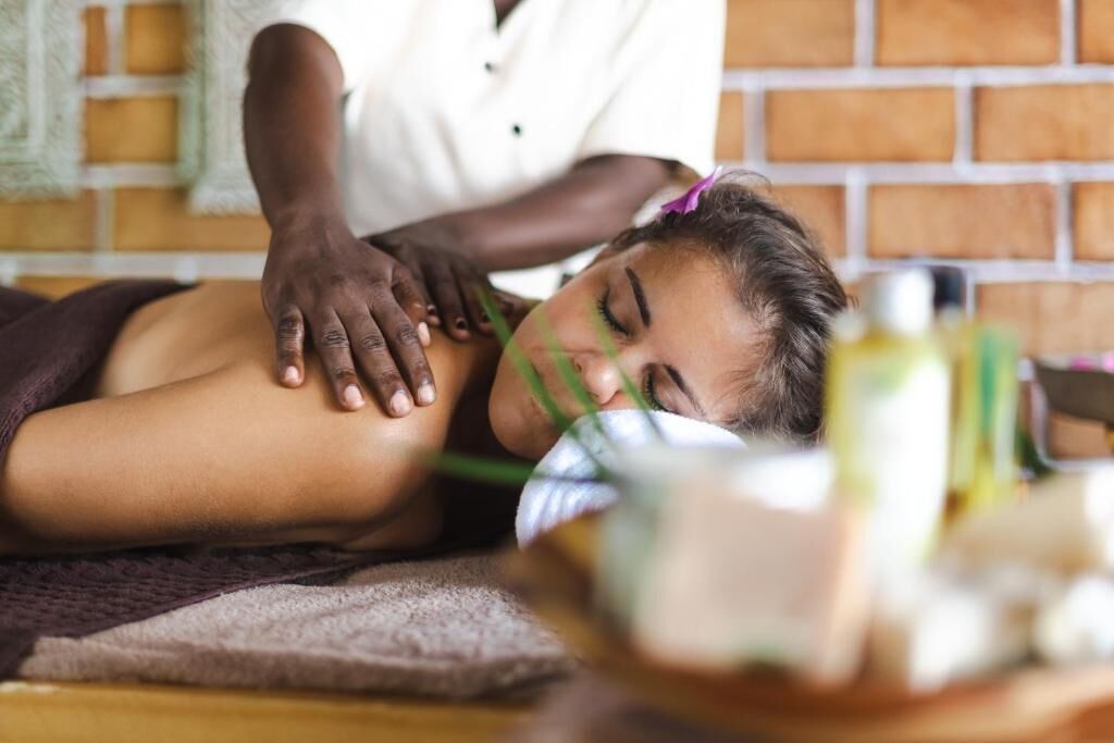 A person receiving a massage in a room with a brick wall and a wooden floor.