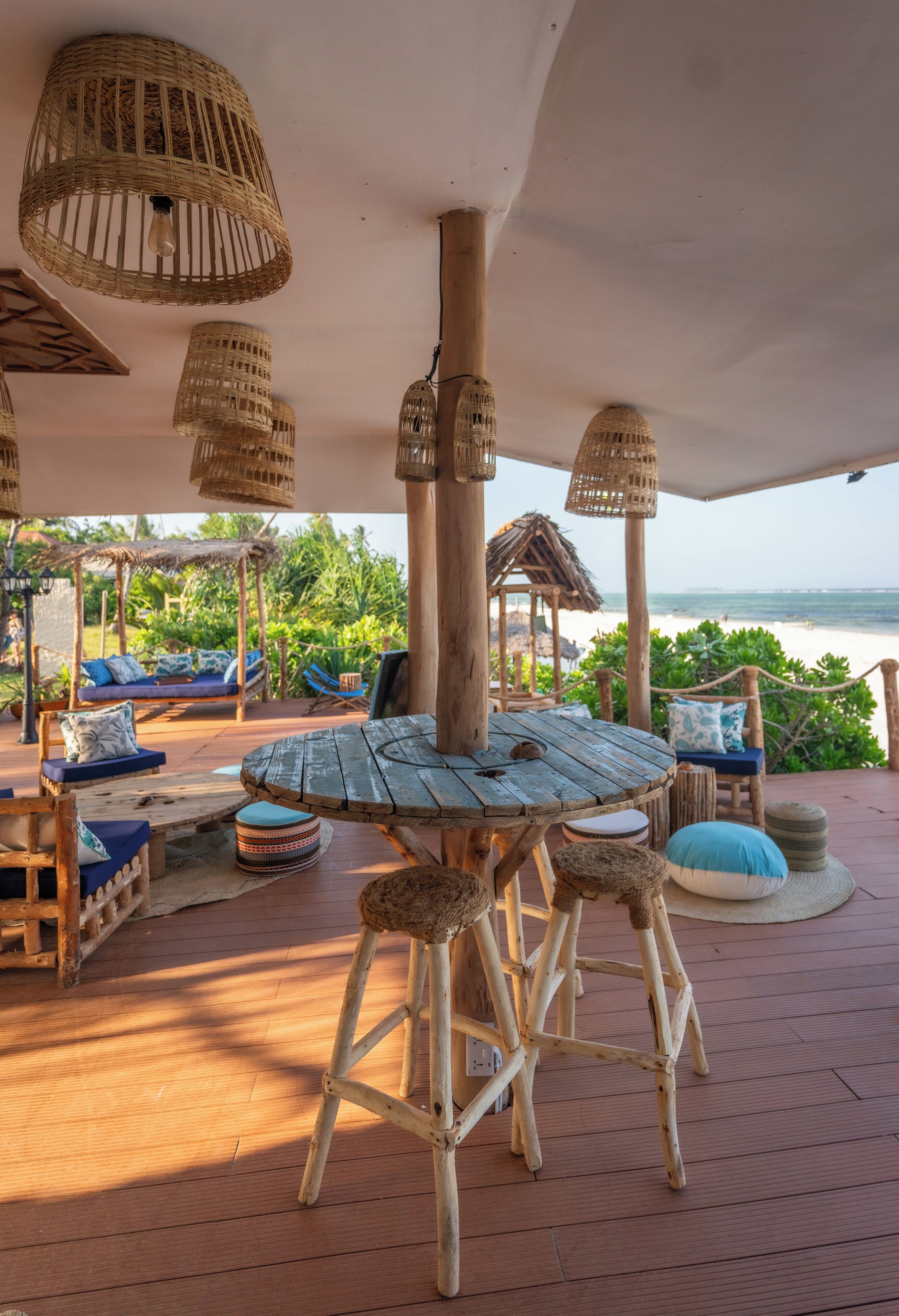 Eine Holzterrasse mit Tisch und Stühlen, einer Hängematte und Blick auf den Strand.