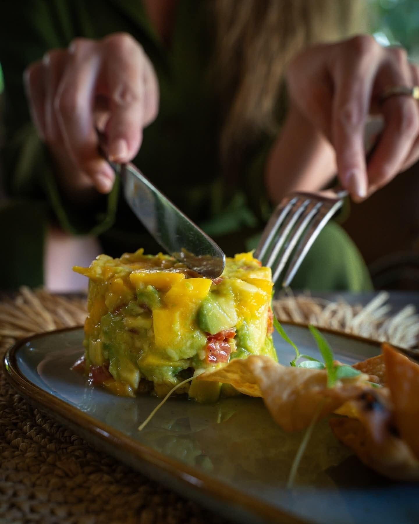 A person cutting a layered dish with a fork and knife.
