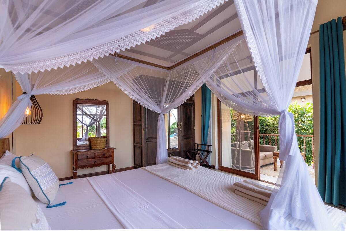 A bedroom with a large bed, a wooden nightstand, a mirror, and a view of the outdoor balcony.