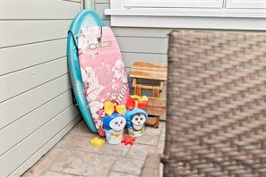 A surfboard leaning against a wall, a small wooden stool, and a woven chair. - Capitola Village Hideaway (Capitola)
