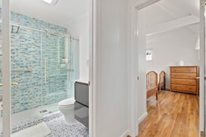 Un baño con cabina de ducha de vidrio, inodoro y cómoda de madera.