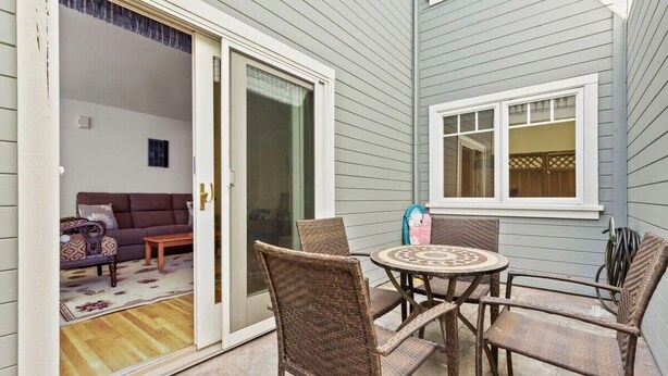 Un espace patio aménagé avec des meubles en osier, une table ronde et une porte-fenêtre coulissante donnant sur un espace de vie intérieur.