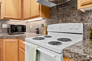 A kitchen with wooden cabinets, a white stove, a microwave, and granite countertops.