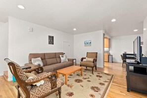 Ein Wohnzimmer mit einer Couch, Sesseln, einem Couchtisch und einem Fernseher.