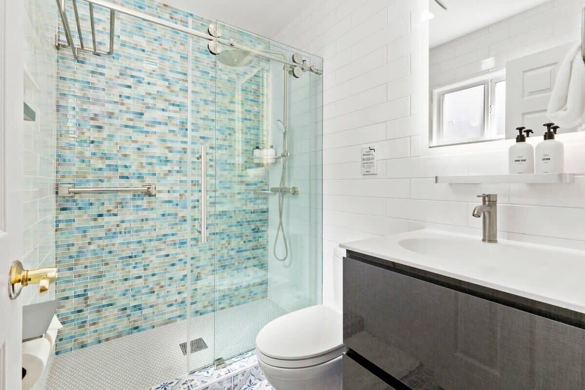 A modern bathroom with a glass-enclosed shower, a white toilet, and a sink with a mirror above it.