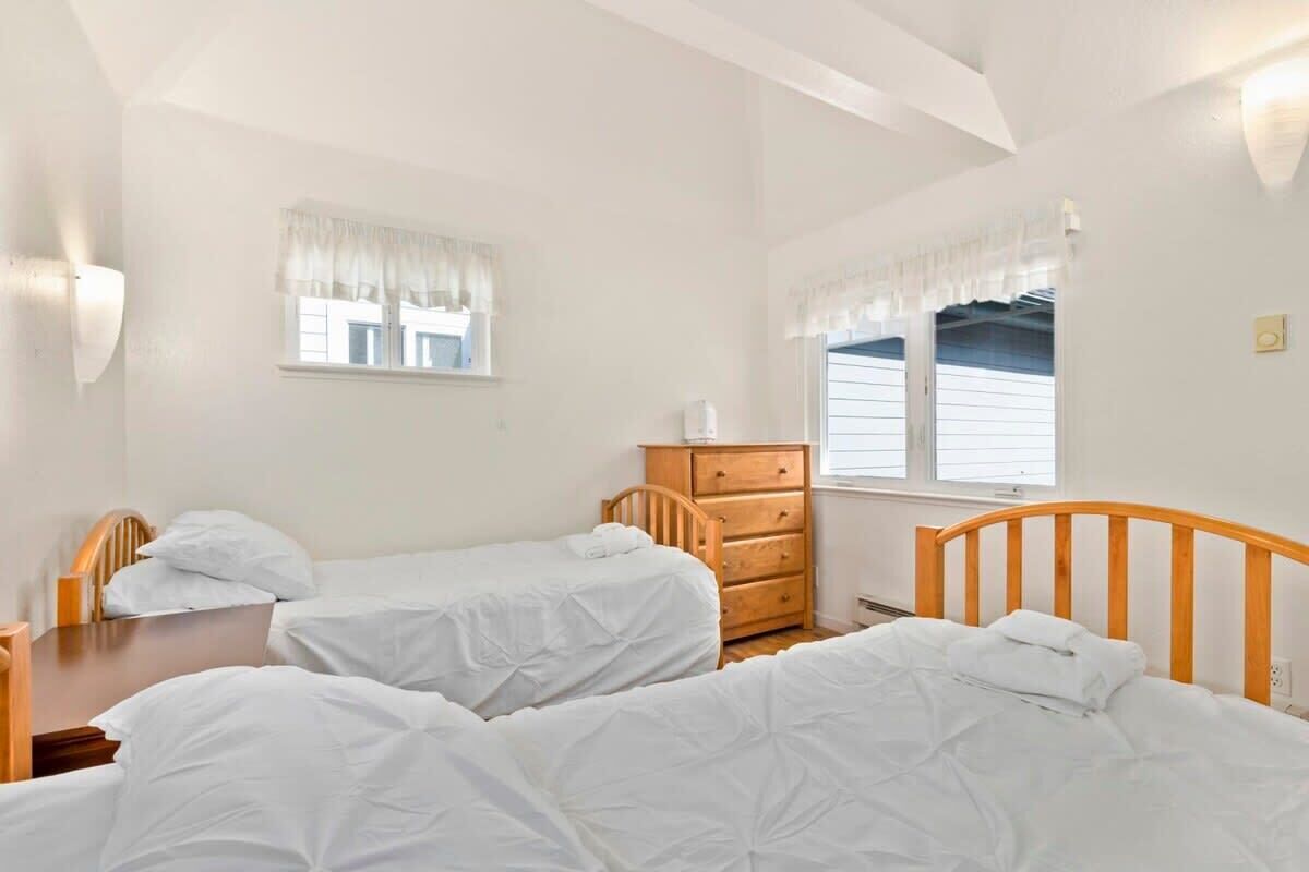 Een kamer met twee enkele bedden, een houten dressoir en een raam met witte gordijnen.