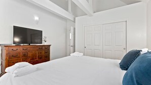 Une chambre à coucher avec un grand lit, une commode en bois, un téléviseur à écran plat et une porte blanche.