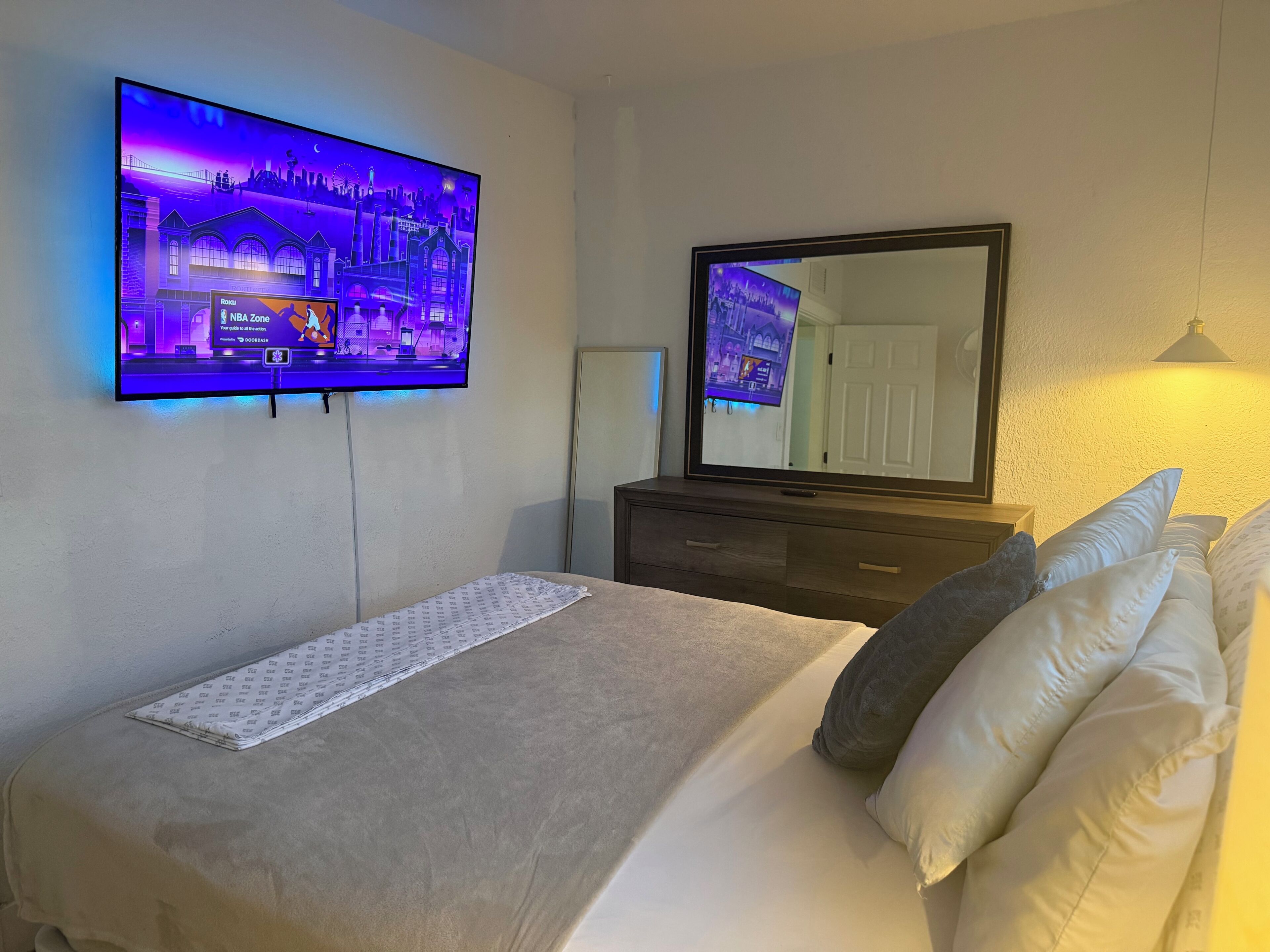 A hotel room with a bed, a TV mounted on the wall, a dresser, and a mirror.