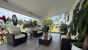 Un espacio de estar al aire libre techado, con mobiliario de mimbre, plantas en macetas y vistas al follaje circundante.