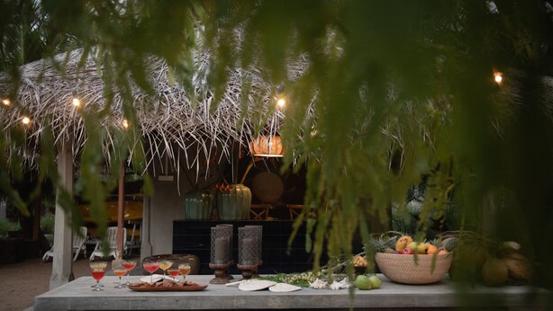 Un área de comedor al aire libre con una mesa dispuesta para una comida, rodeada de follaje e iluminación decorativa.