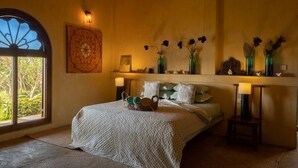 Un dormitorio con una cama grande, una ventana con vistas decorativas, un estante con jarrones y una lámpara, y una obra de arte colgada en la pared.
