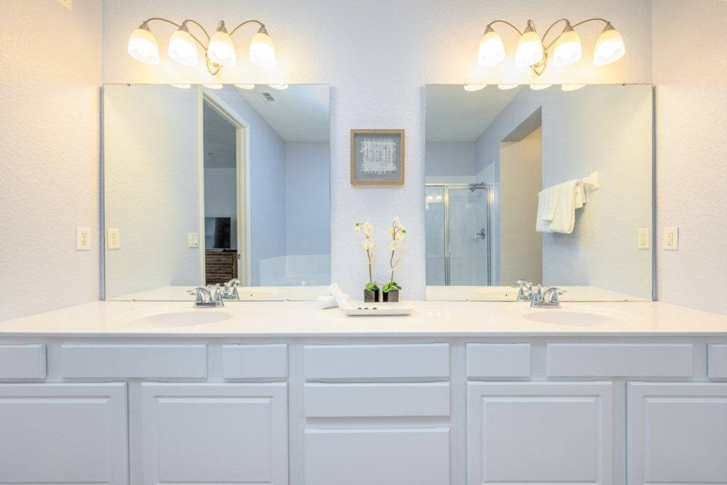 A bathroom with a double sink vanity, two wall-mounted light fixtures, a framed picture, and a small potted plant.