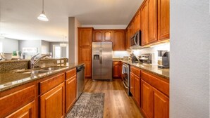 Une cuisine moderne dotée de meubles en bois, d’appareils électroménagers en acier inoxydable, de plans de travail en granit et de luminaires suspendus.