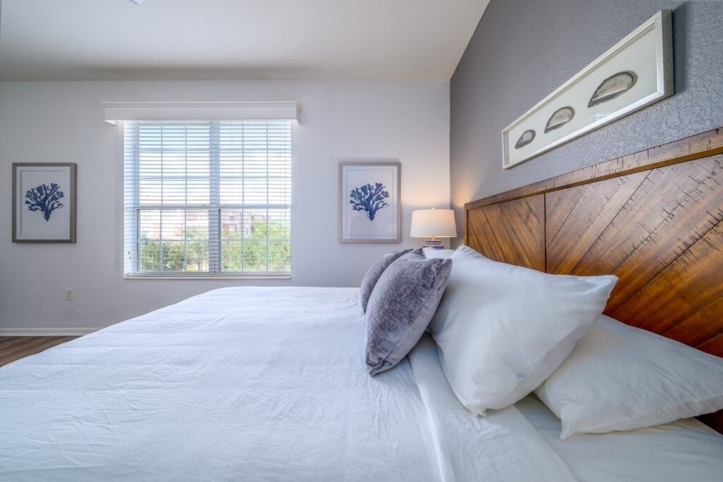 A bedroom with a large bed, a window with blinds, and framed artwork on the wall.