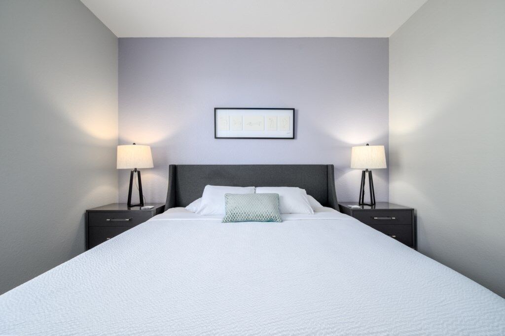 A hotel room with a large bed, two bedside tables, a framed picture on the wall, and two lamps.