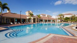A swimming pool with lounge chairs and umbrellas, surrounded by buildings with a Mediterranean architectural style. - Vista Cay Lakeview Elysium 3 Bedroom Condo by RedAwning (Orlando)