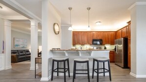 A modern kitchen with wooden cabinets, a stainless steel refrigerator, and a bar area with stools. - Vista Cay Lakeview Elysium 3 Bedroom Condo by RedAwning (Orlando)