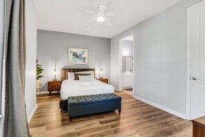 Un dormitorio con cama, mesitas de noche, ventilador de techo y un ventanal grande.