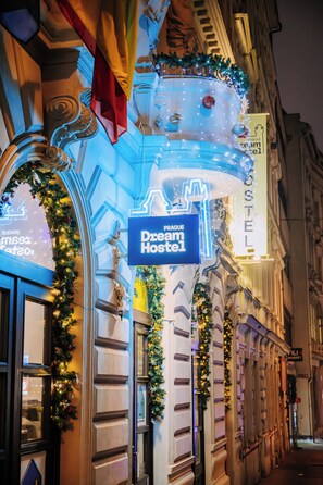 Fachada de edifício com letreiro de neon do Dream Hostel, decorada com guirlandas e luzes festivas.