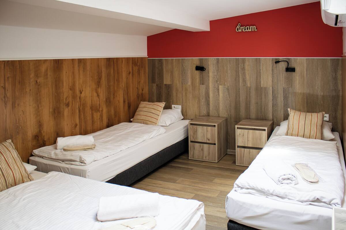 A hotel room with three beds, wooden paneling on the walls, and a red accent wall with the word "dream" on it.