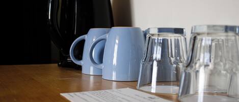 A table with a coffee maker, two blue mugs, and a glass pitcher.