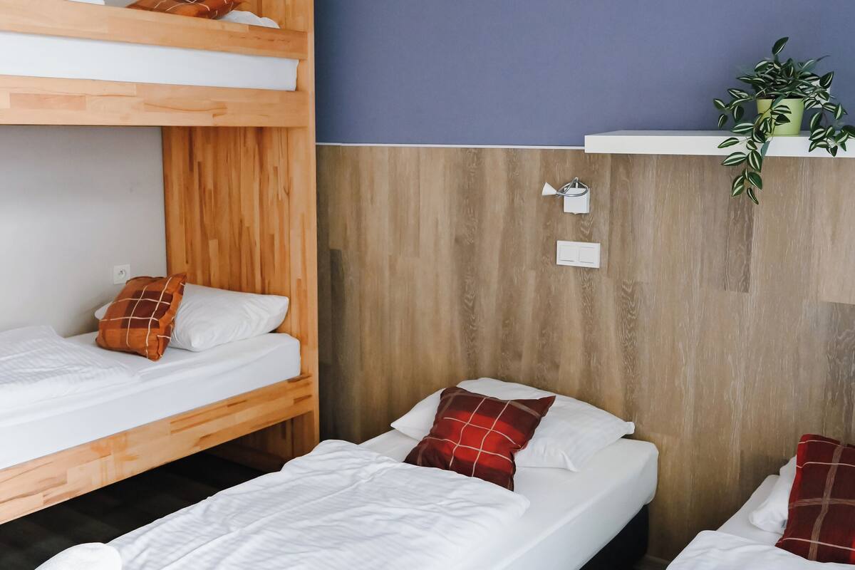 A room with two single beds, a bunk bed, and a small shelf with a plant.