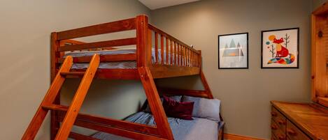 A bunk bed with a wooden ladder, a single bed with pillows, a dresser, and two framed pictures on the wall.