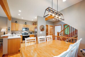 A modern kitchen with wooden cabinets, stainless steel appliances, and a dining area with a wooden table and white chairs. - Cozy Rustic Duplex w/ Hot Tub, Fireplace & Views (McHenry)
