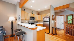 A modern kitchen with wooden cabinets, stainless steel appliances, a bar area, and a staircase leading to another level. - Cozy Rustic Duplex w/ Hot Tub, Fireplace & Views (McHenry)