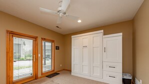A room with a ceiling fan, two sliding glass doors with blinds, a white wardrobe, and a carpeted floor.
