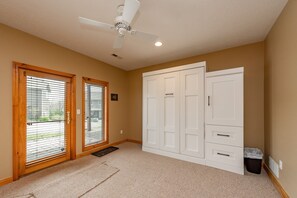 A room with a ceiling fan, two sliding glass doors with blinds, a white wardrobe, and a carpeted floor. - Cozy Rustic Duplex w/ Hot Tub, Fireplace & Views (McHenry)