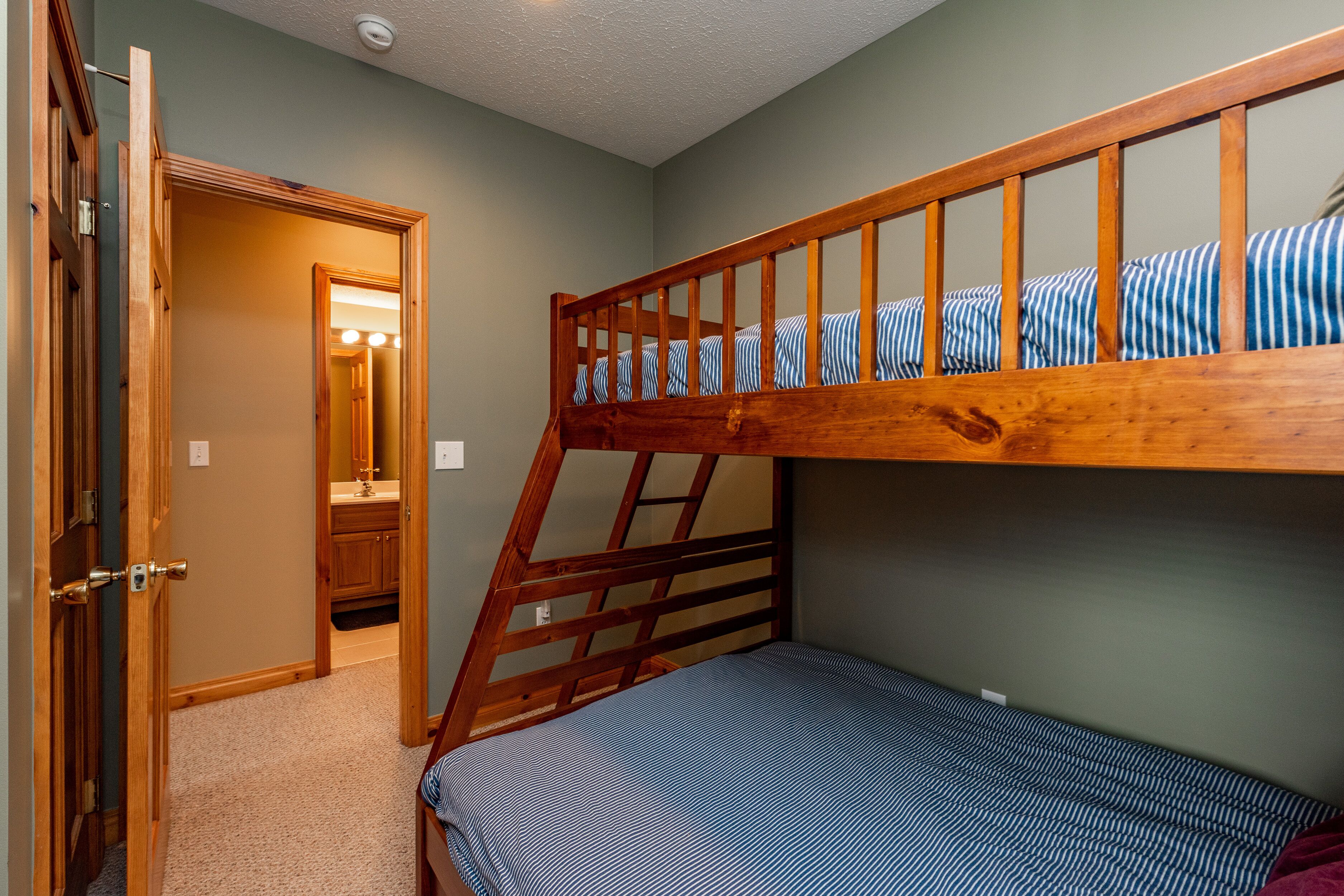 A bedroom with a bunk bed, a door leading to a bathroom, and a carpeted floor.