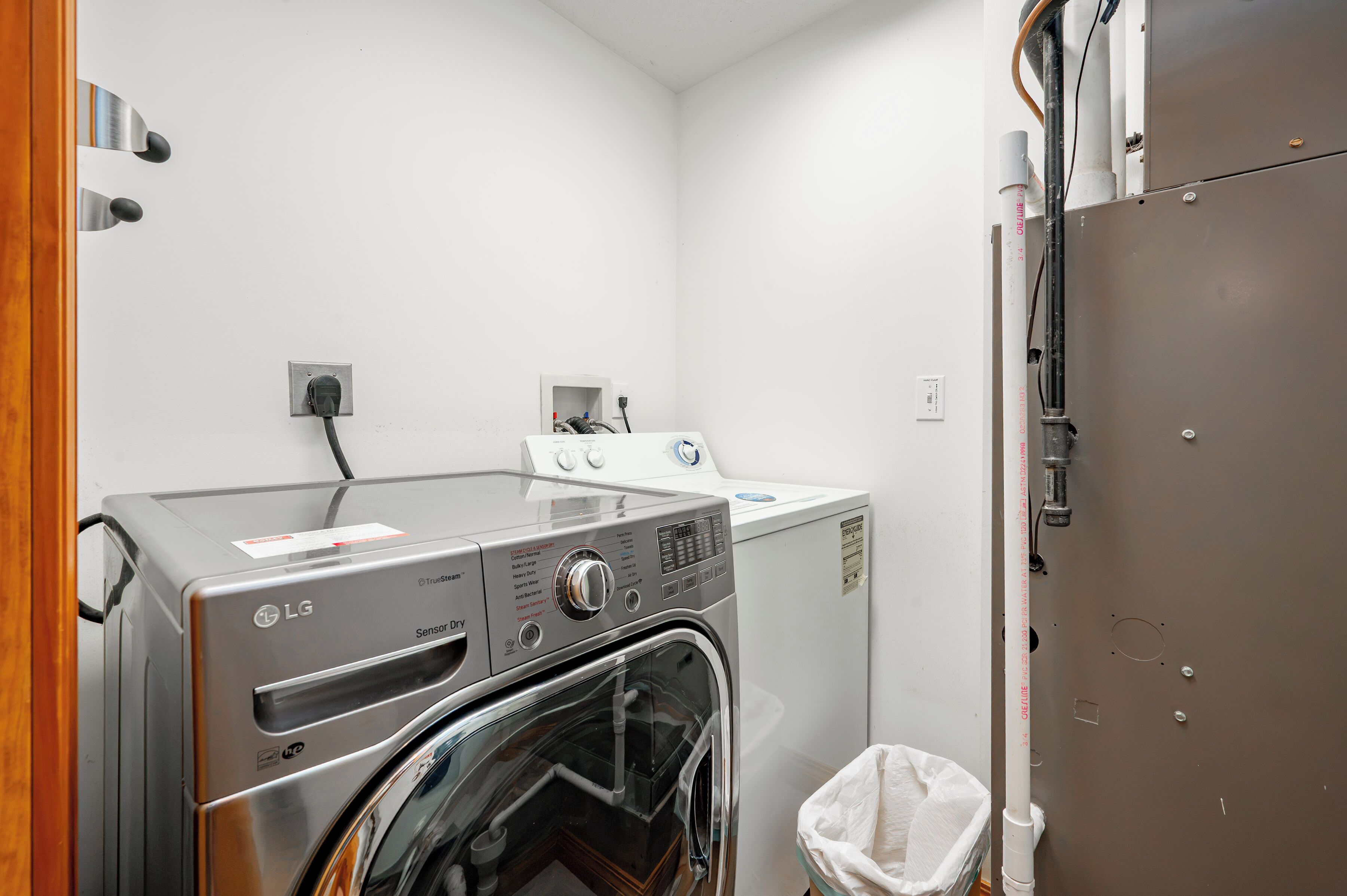 A laundry room with an LG Sensor Dry washer and dryer, a white wall, and a wooden door.