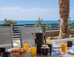 Desayuno con jugo de naranja, café y pasteles sobre una mesa con vista al océano.