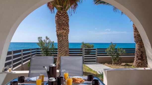 A breakfast table with a view of the sea, a palm tree, and a clear sky. - Atalanti Seaside Junior Suites (Viannos)