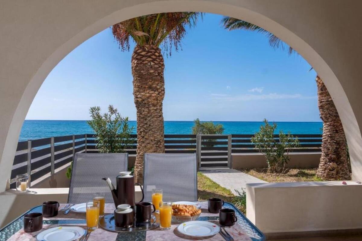 Mesa de café da manhã com vista para o mar, uma palmeira e céu claro.